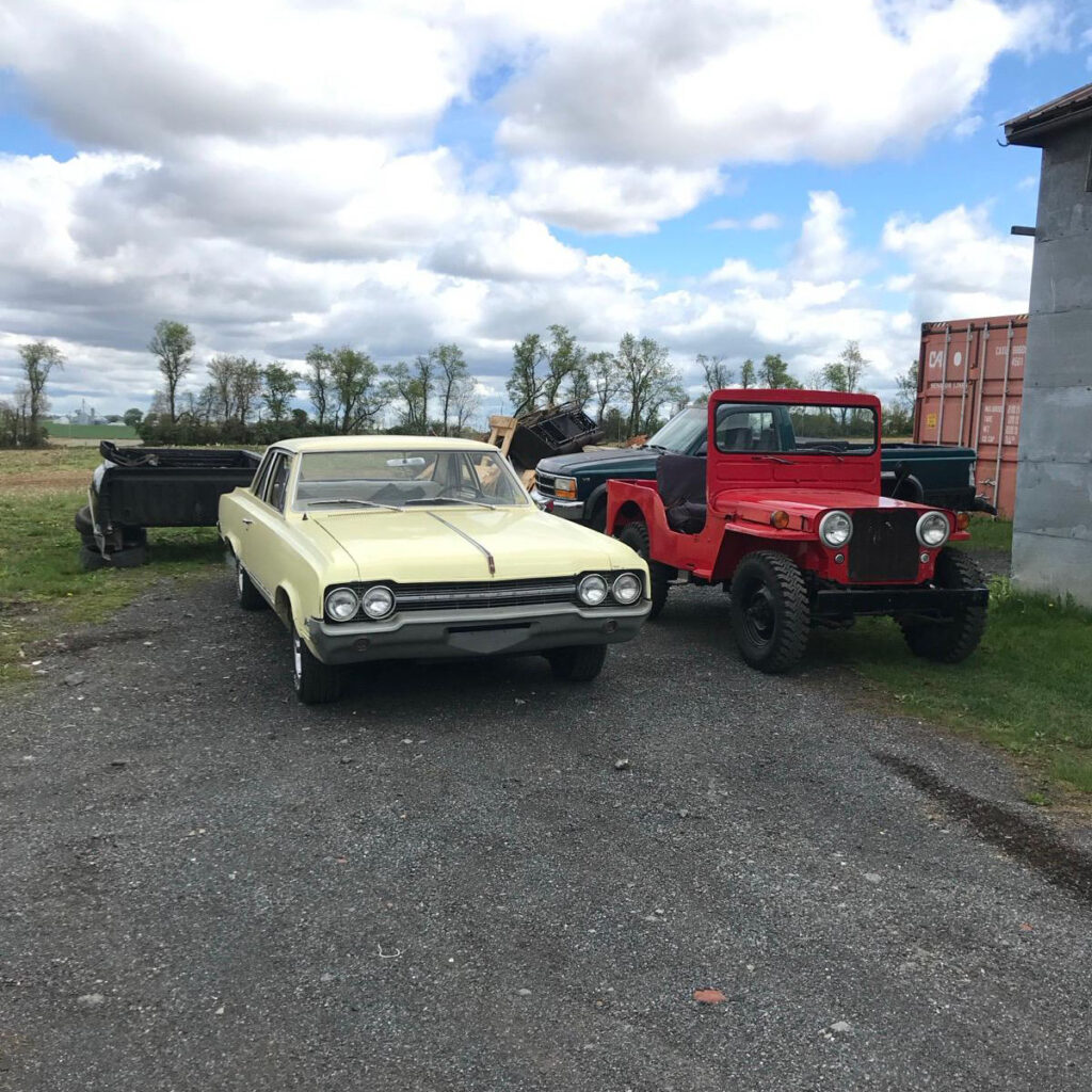 An off-white vintage car in Restored Auto's parking lot