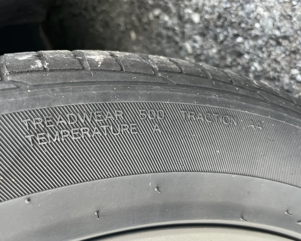 A photo of a tire with a treadwear, traction, and temperature code that says "TREADWEAR 500 TRACTION AA TEMPERATURE A"