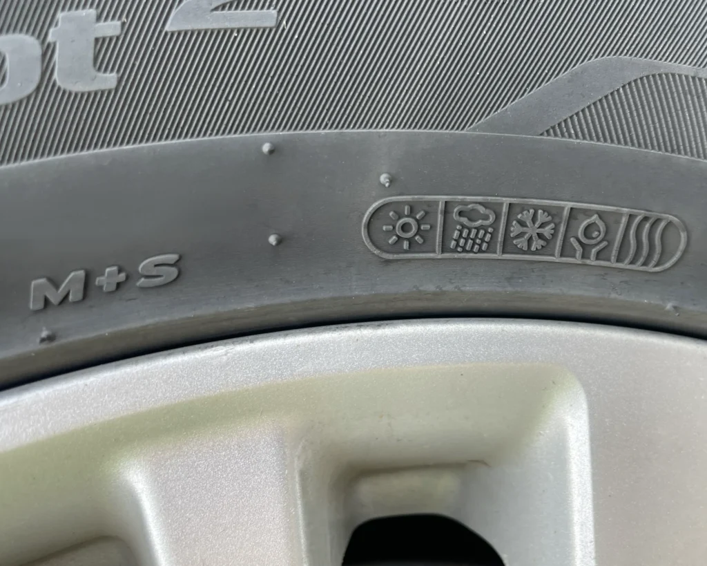 A photo of a tire with weather codes that say "M+S" and have icons of a sun, a rain cloud, a snow flake, an eco icon, and a water icon