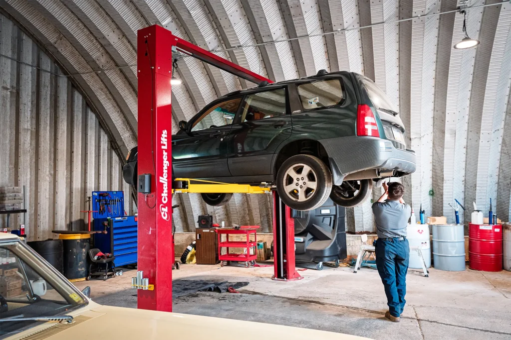 A Restored Auto mechanic standing near a car on a lift